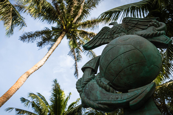 A close up of the Eagle Globe and Anchor statue in front of palm trees.