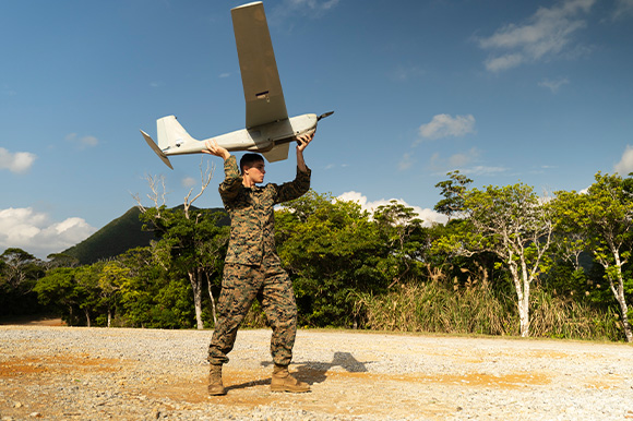 A Marine outside holding up a large drone shaped as an airplane.