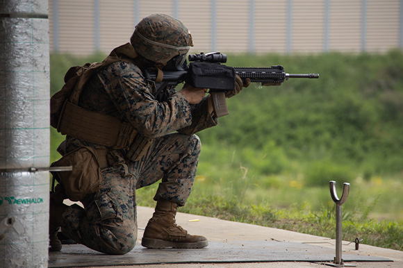 A Marine in combat uniform aiming a gun to the right.