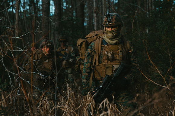Marines in combat gear walking in dark woods.