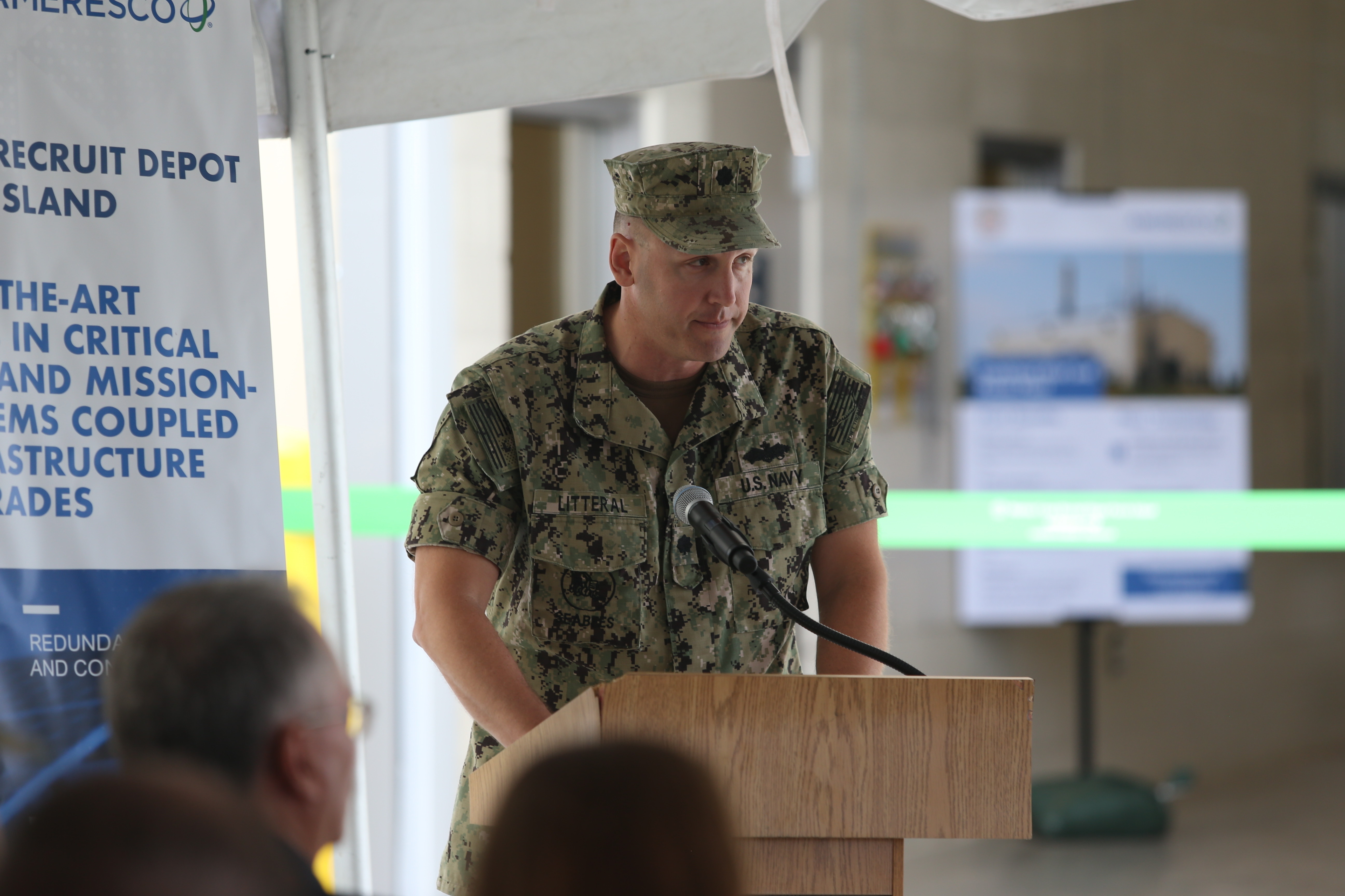 A Marine in uniform leaning over a podium facing a crowd of people.