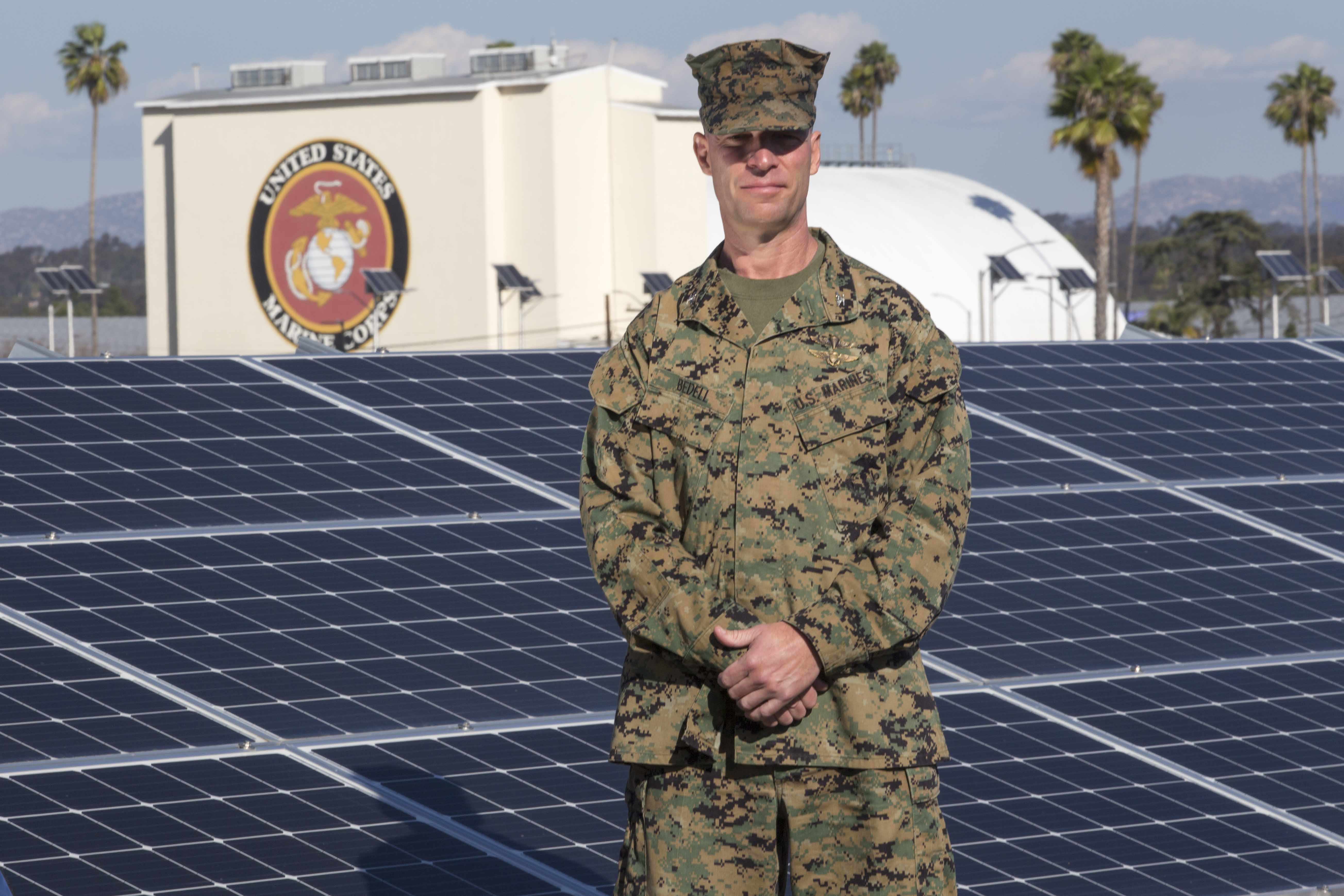 A Marine in uniform posing in front of a giant solar panel.