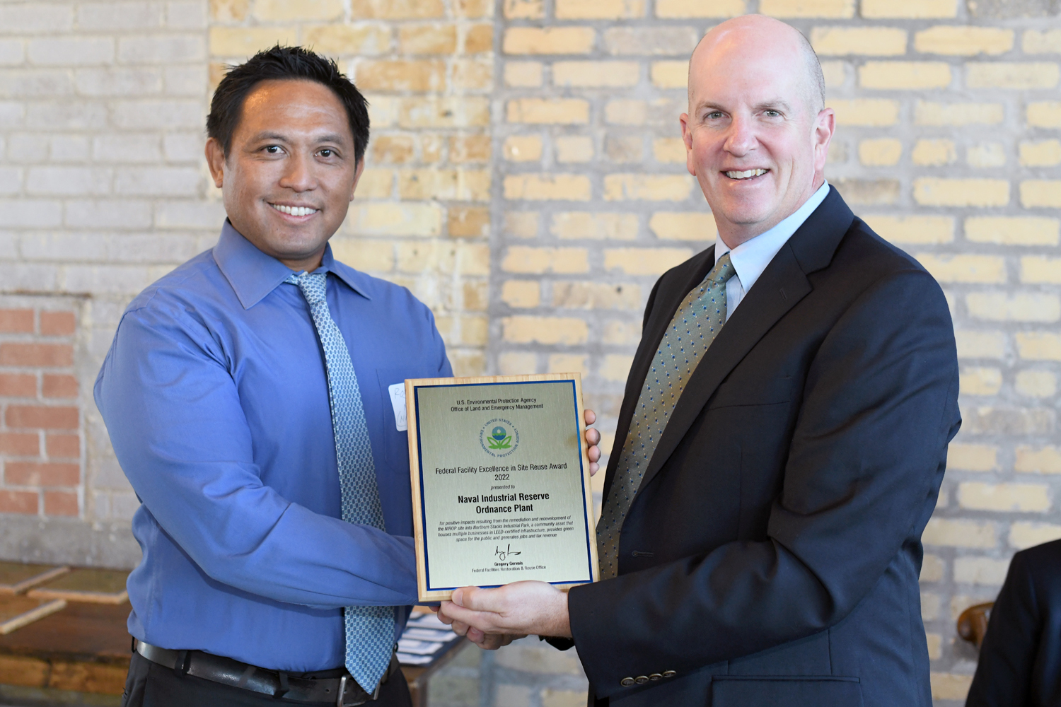 Two men in business wear, shaking hands while one receives an award plaque.